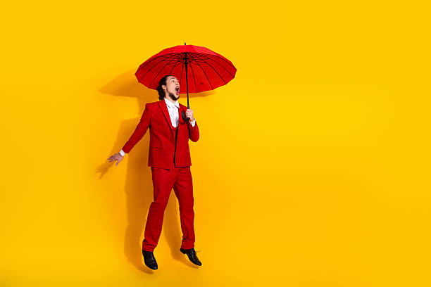 istock Funny bold man in red suit and umbrella leaps against a bright yellow background creating glamorous stylish fashion moment for holiday and advertisement 2238044246