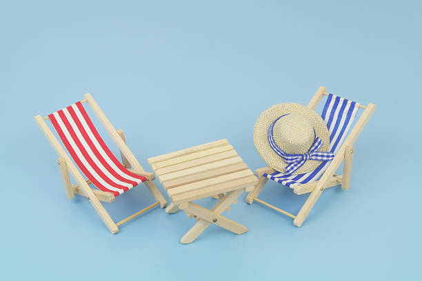 Blue and red beach chairs with hat and wooden table on blue background. Copy space for text. Travel and vacation concept.
