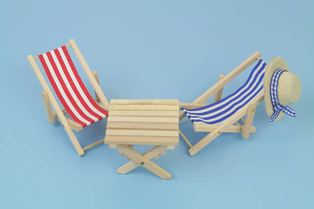 Blue and red beach chairs with hat and wooden table on blue background. Copy space for text. Travel and vacation concept.
