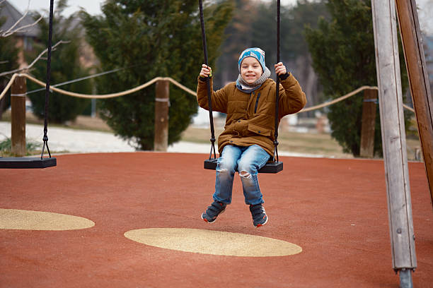 Happy boy swinging on a swing at a playground, enjoying outdoor recreation in winter.