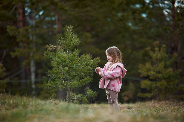 Young girl smiling and watching a small pine tree in nature.