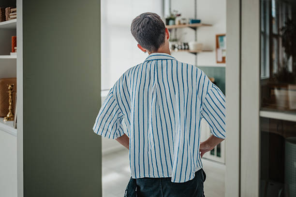 Young woman standing with hands on hips, appearing bored and unmotivated while looking at dirty dishes in kitchen.
