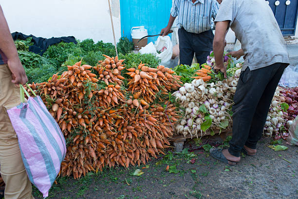 Unrecognizable sellers arranging organic carrots and turnips. Douz market, Tunisia