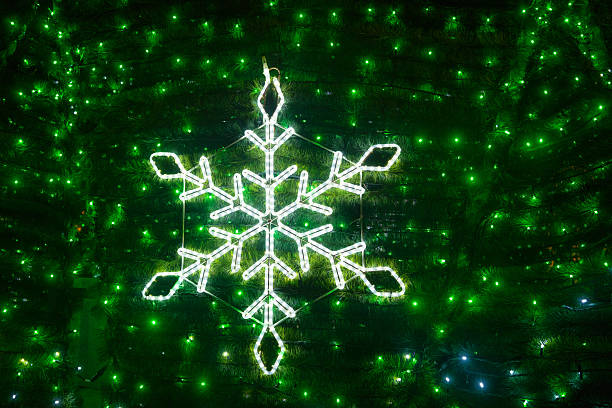 Bright snowflake shape with green lights on evergreen branches at night