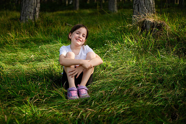 Young girl smiling and sitting on green grass in a forest, enjoying nature and summer leisure activities