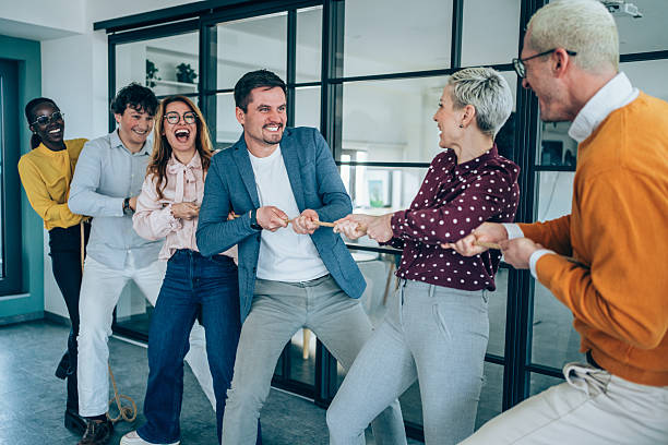 istock Playful colleagues having fun while playing tug-of-war in the office. 2238058382