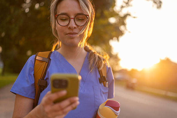 istock Focused female nurse in uniform using phone outdoors during sunset going for job 2238061255