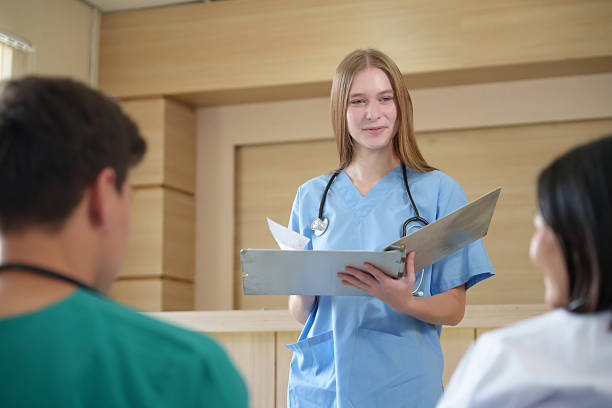 istock Smiling young nurse wearing blue scrub standing with folder, presenting treatment plan to doctor team during hospital discussion. 2238062314