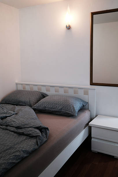 istock Cozy bedroom with patterned bedding, wooden floor, bedside table and a glowing wall lamp. The minimalistic interior of the hotel. 2238067119