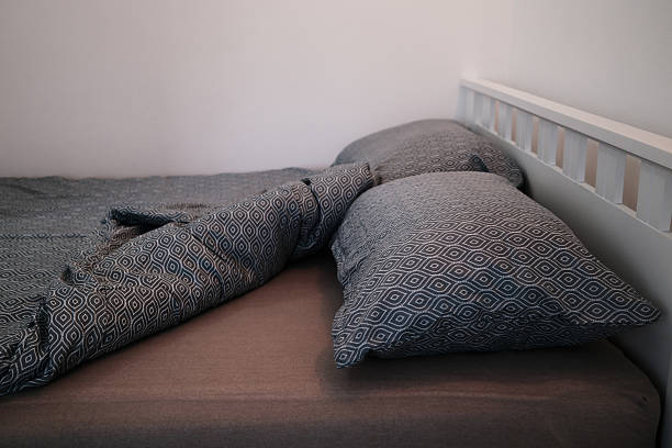 Crumpled patterned blanket and pillows on an unmade bed, capturing a lived-in atmosphere. Cozy bedroom design of a country house or hotel