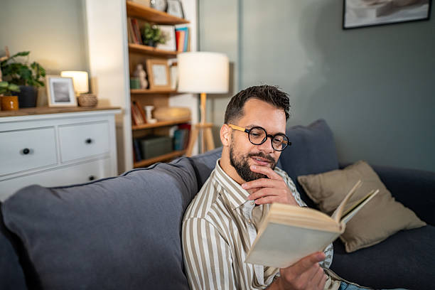 istock Man relaxing on sofa reading book in living room 2238070754