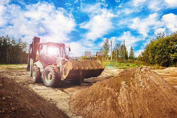 istock Backhoe loader collects sandy material from high pile, transporting loose earth toward open space between several uneven mounds. 2238072998