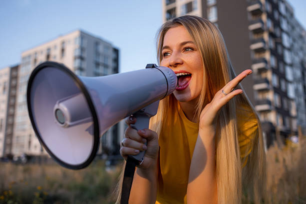 istock Cheerful woman outdoors using megaphone during a sunny day near buildings. 2238078413