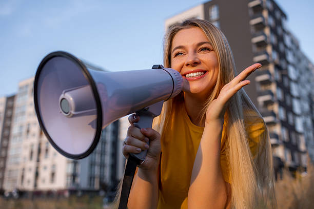 istock Joyful woman using a megaphone outdoors with modern buildings in the background 2238078420