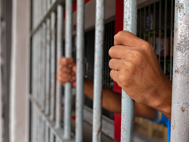 istock prisoner's hands behind bars with black background 2238078468