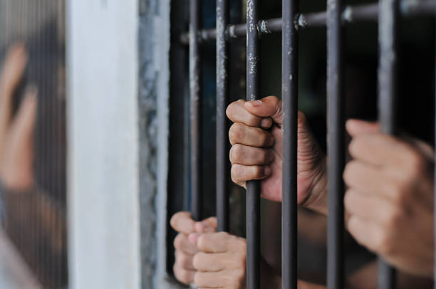istock prisoner's hands behind bars with black background 2238079654