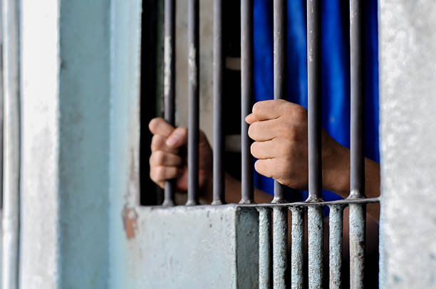 istock prisoner's hands behind bars with black background 2238079695