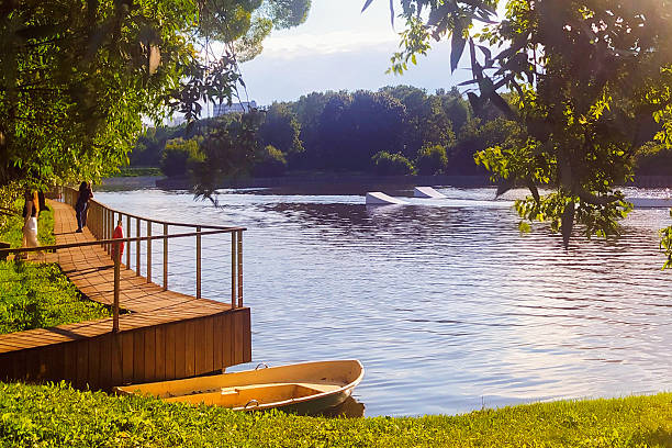 Wooden pier by calm river with moored boat, lush trees, and golden sunlight. Peaceful nature scenery symbolizing relaxation, eco tourism, countryside, and slow living.