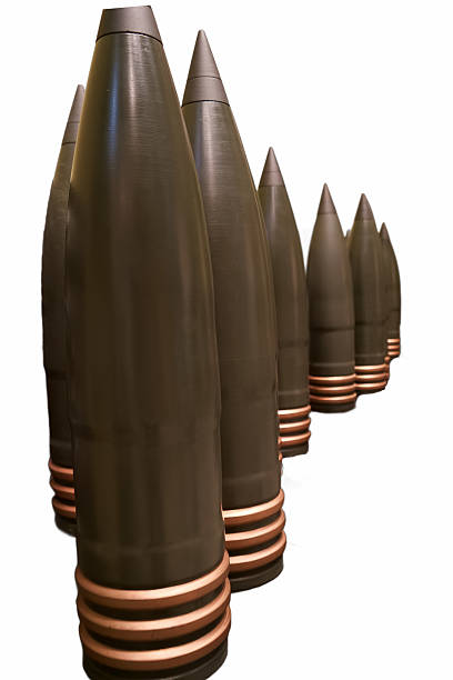 Heavy artillery shells stand in a straight line, displaying their sleek design. The shells have a dark surface with distinctive copper banding, reflecting military engineering.