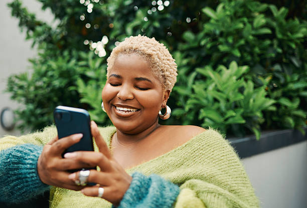istock Smiling Blonde Woman in Green Sweater Using Smartphone Outdoors Among Lush Greenery 2238106963