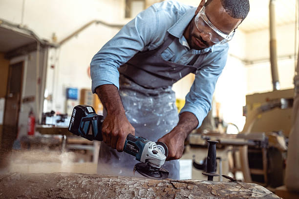 istock Focused Multiracial Artist Sculpting a Wooden Log in a Well-Lit Workshop Using Power Tools 2238108088