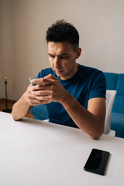 istock Vertical shot of focused male in casual clothes using mobile phone sitting at table, browsing internet or social media, concentrating on online content at home. 2238108459