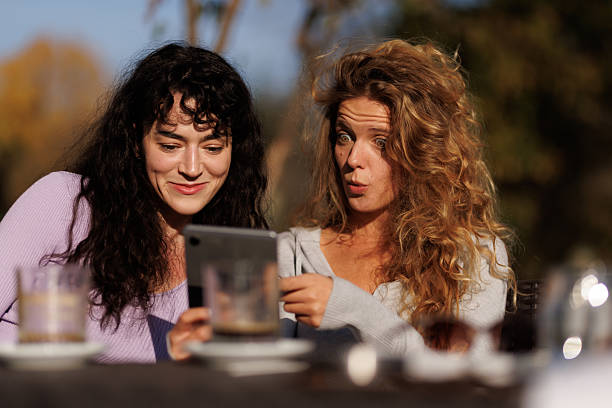 istock Two friends sharing a joyful moment while enjoying drinks and looking at a tablet outdoors in a cozy setting with fall colors in the background 2238108737