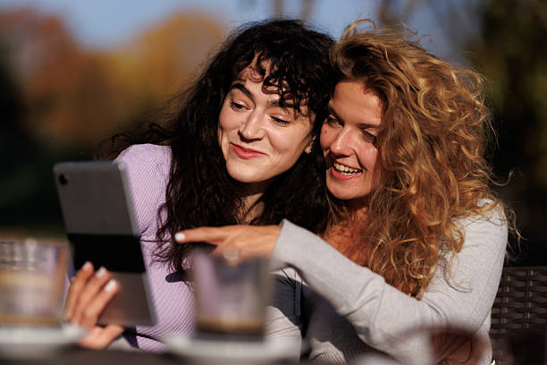 istock Friends enjoying a sunny day outdoors while sharing smiles and laughter, captivated by a device, surrounded by nature and autumn colors 2238108742