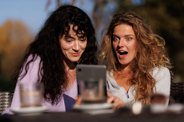 istock Two friends enjoying a sunny day outdoors as they share excitement while looking at a tablet in a park setting during late afternoon 2238108751