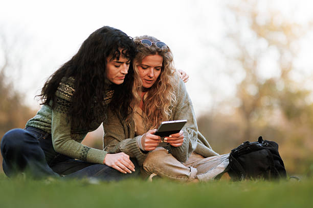 istock Two friends enjoying a moment outdoors while looking at a device during a sunny afternoon in the park 2238108817