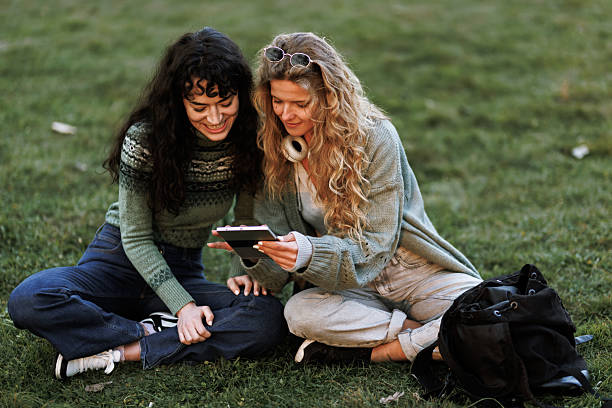 istock Friends enjoying a sunny day outdoors, sharing laughter while using a tablet on the grass at a park in the afternoon 2238108821