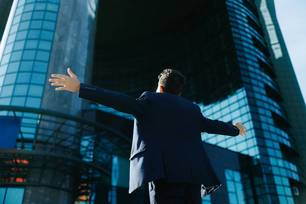 istock back view Young professional in suit raising arms with joy in modern city 2238111445