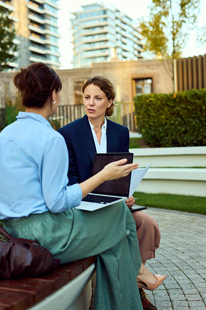 istock Professional Women Discussing Project Outdoors With Laptop And Documents In Urban Park Setting 2238112423