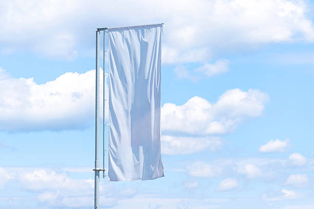 istock Single tall vertical white banner on pole fluttering in wind with cloudy blue sky background, outdoor advertising space 2238112453