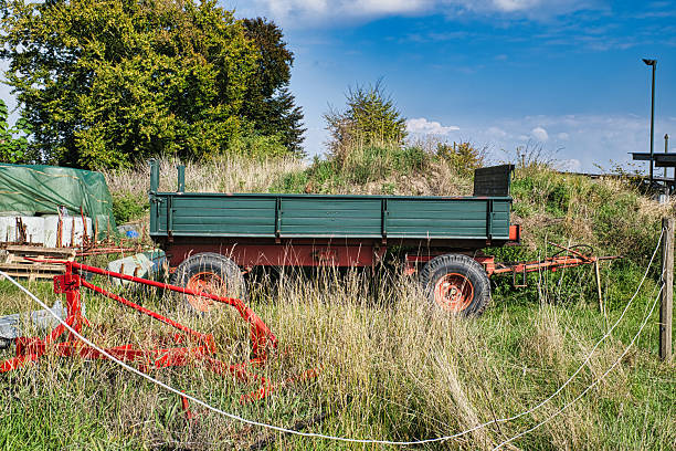 Old farm trailer in tall grass field under blue summer sky