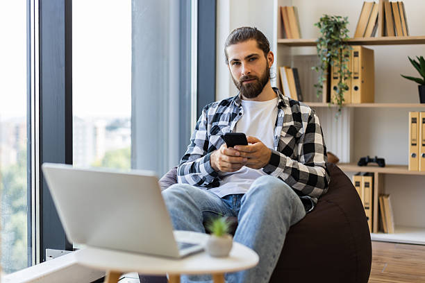 istock Young man with smartphone working remotely in modern bright office space 2238114449