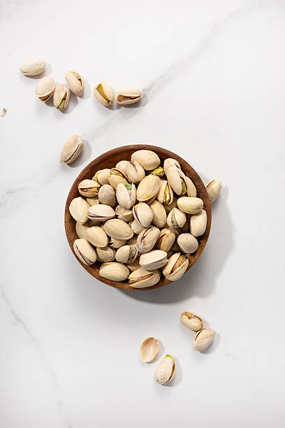 istock Overhead view of pistachio nuts in bowl on light surface 2238118312