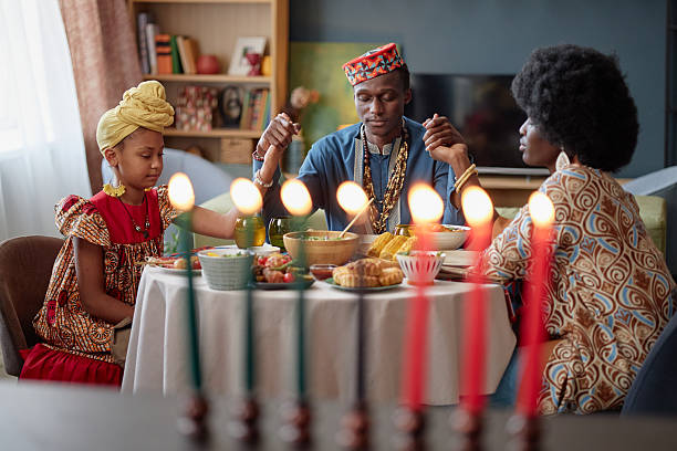 istock Black Family Celebrating Kwanzaa Holding Hands Around Dinner Table 2238119789