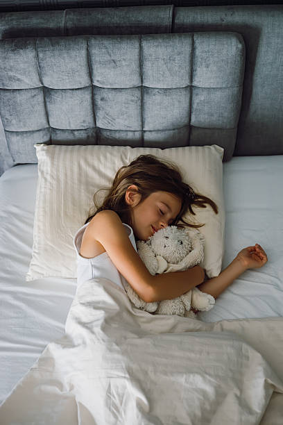 istock Young girl sleeping peacefully in a comfortable bed, hugging a white stuffed bunny toy, high angle shot 2238120058
