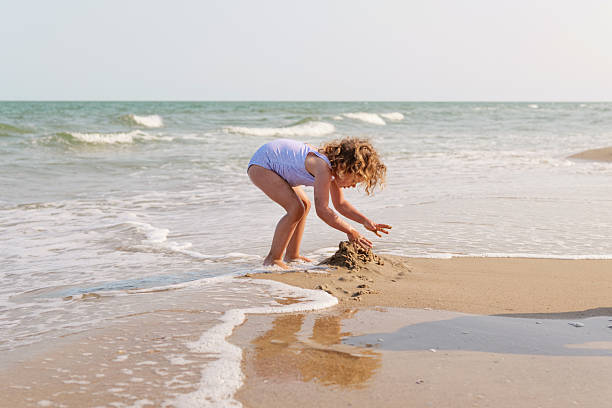istock A joyful child plays at the shoreline, crafting a sandcastle while waves gently lap at her feet during a bright day 2238122694