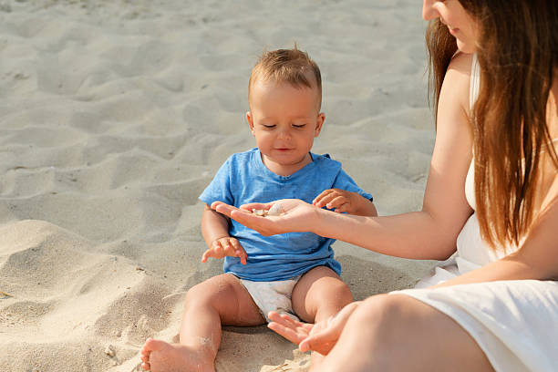 istock A delighted toddler sits on warm sand while an adult shares small shells, creating a fun learning experience on a bright beach day 2238122696
