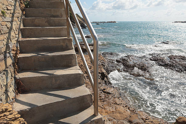 Stone path with iron railings leading to sea on sunny summer day. Nature and buildings.