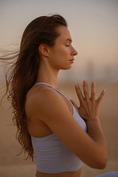 istock Woman meditating on a beach at sunset with hands in prayer and serene expression 2238127152
