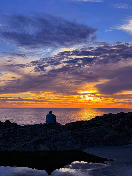 istock Sunset sky over the sea and a lonely man sitting on the shore. 2238127708