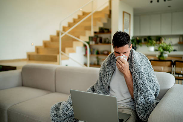 istock Sick australian mid adult man blowing nose while using laptop at home 2238130883