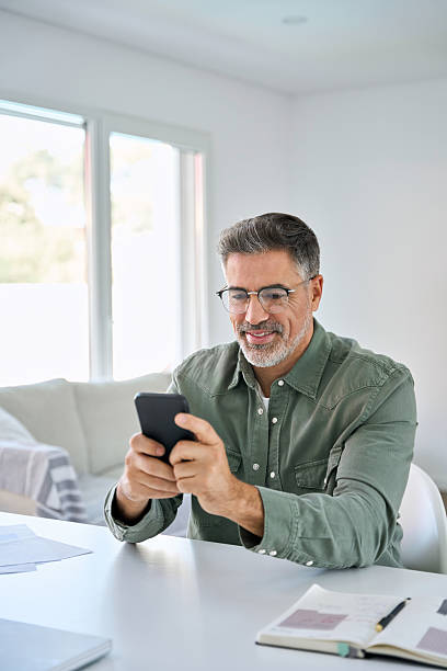 istock Happy middle aged man using mobile cell phone sitting at home table. Vertical. 2238131336