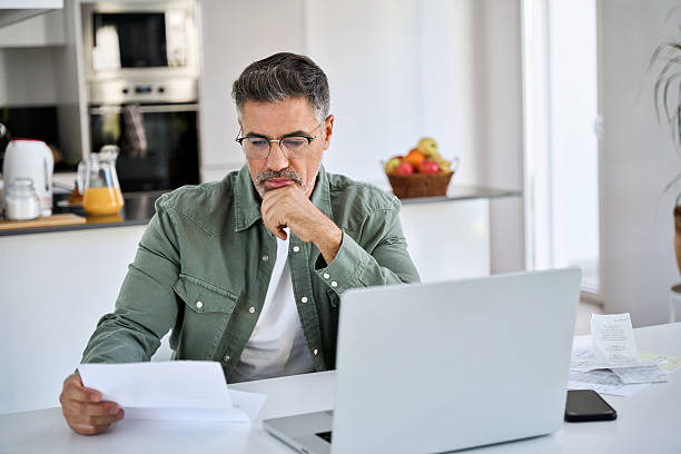 istock Worried mature man looking at bill working at home kitchen using laptop. 2238131349