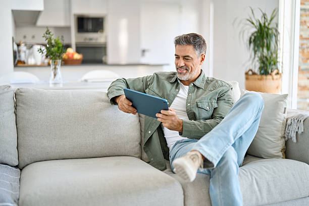 istock Happy middle aged man using digital tablet relaxing on couch at home. 2238131381