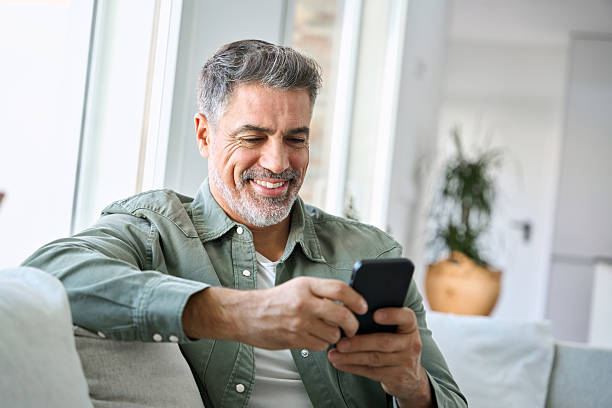 istock Smiling mature middle aged man using mobile phone sitting at home on couch. 2238131384