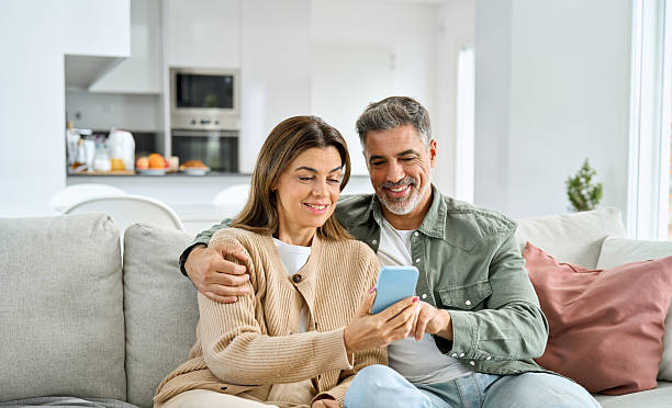 istock Happy older mature couple using smartphone sitting at home relaxing on couch. 2238131427